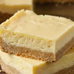 Stacked carnivore cheesecake bars with a buttery crust and creamy zero-carb filling, cut from a glass baking dish.