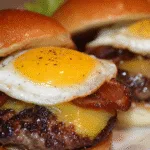 Close-up of fried egg bacon cheeseburger sliders with juicy beef patties, melted cheese, crispy beef bacon, and sunny-side-up eggs on toasted brioche buns